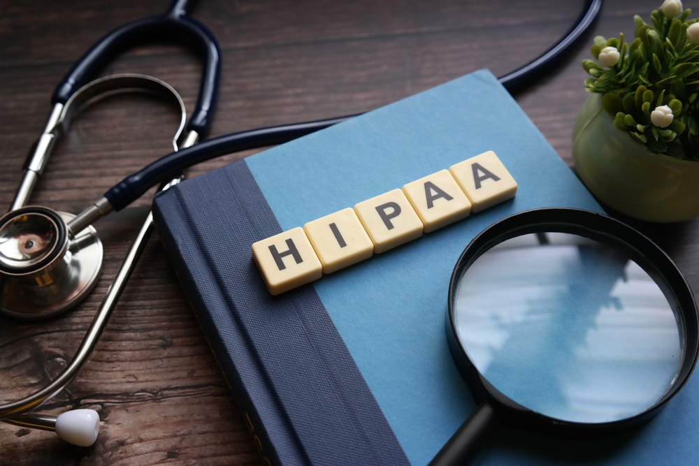 Closeup of a stethoscope and notebook on a table with the word HIPAA